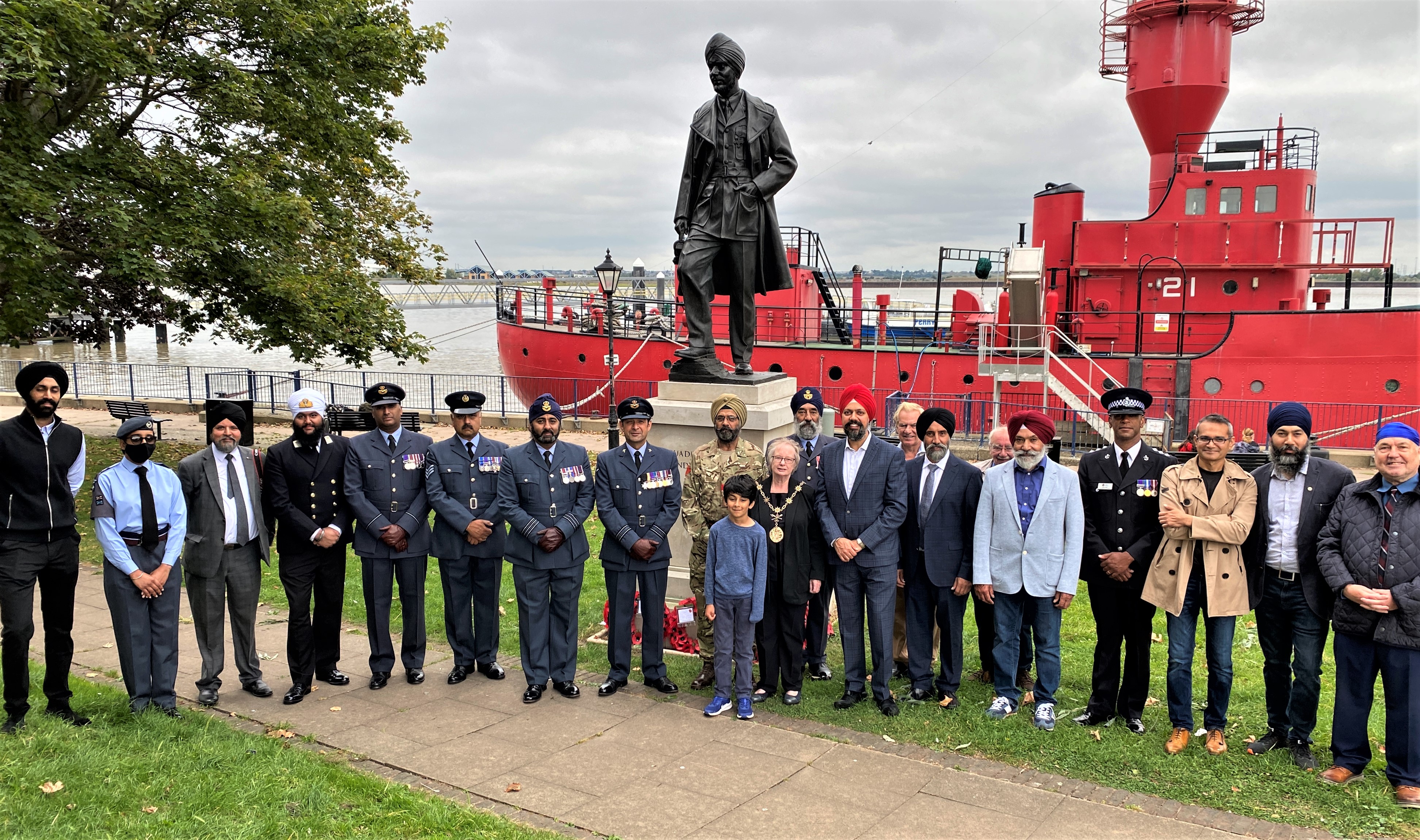 Personnel in Sikh attire stand by the statue and boat on the water.
